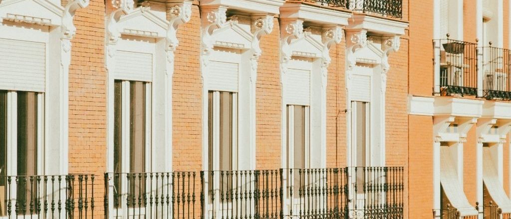 A terracotta facade of shuttered windows and iron balconies, repeating along the street