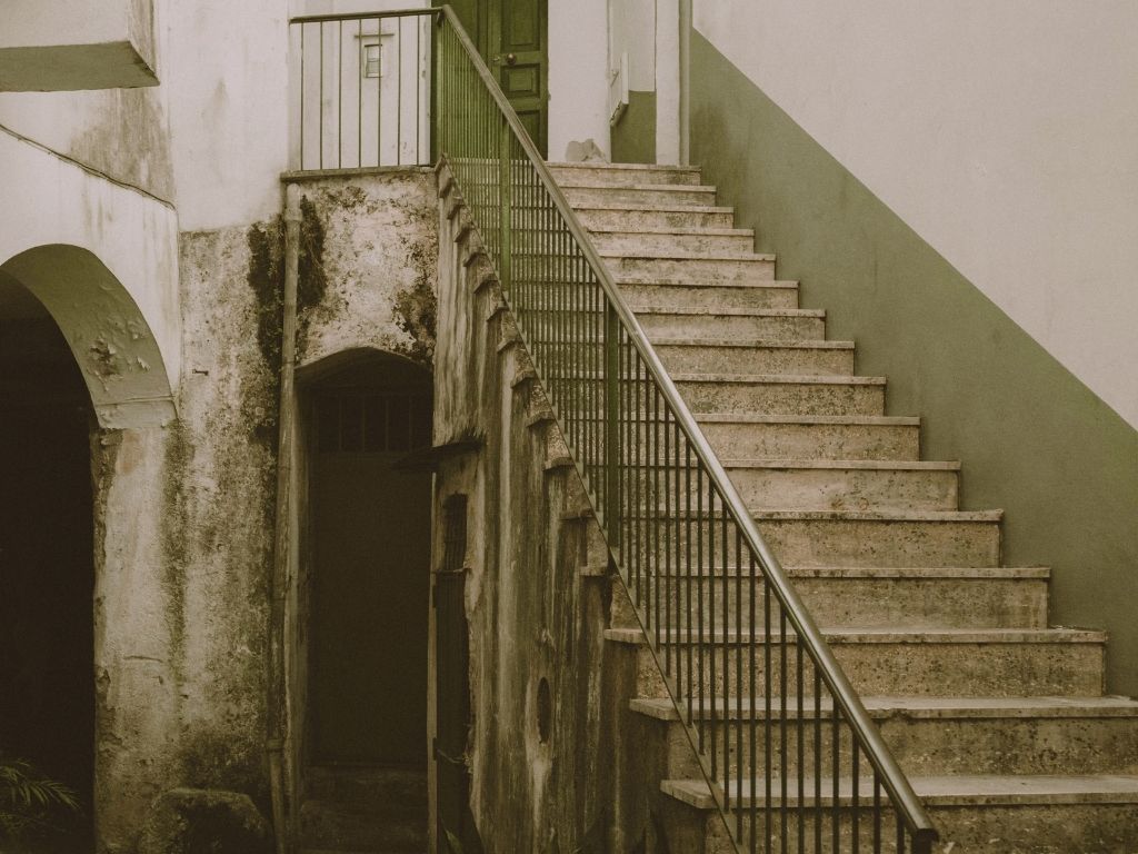 A stone staircase climbing between walls with a plain iron railing