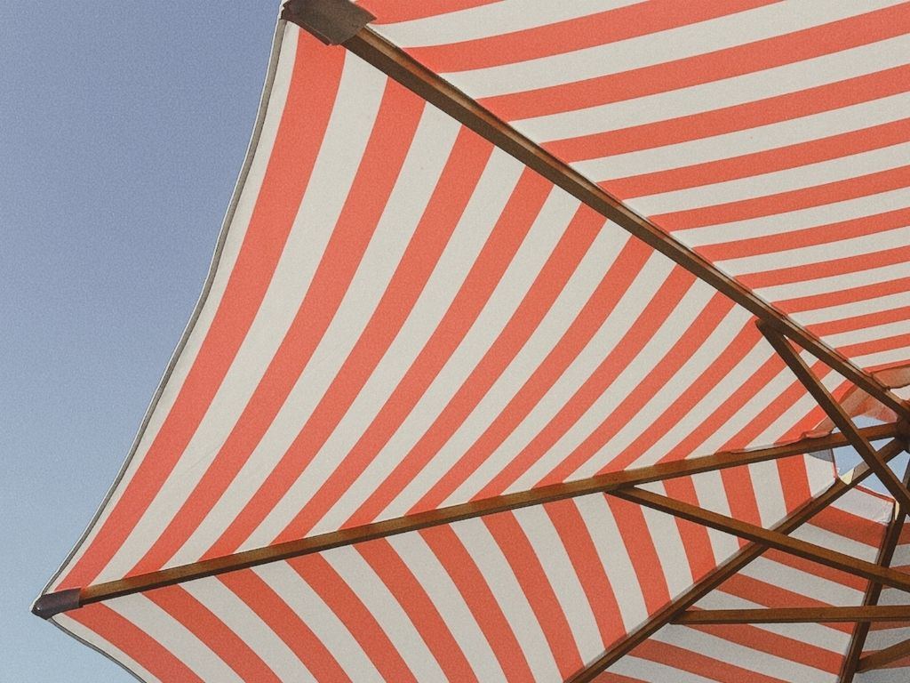 A red and white striped umbrella against a blue sky